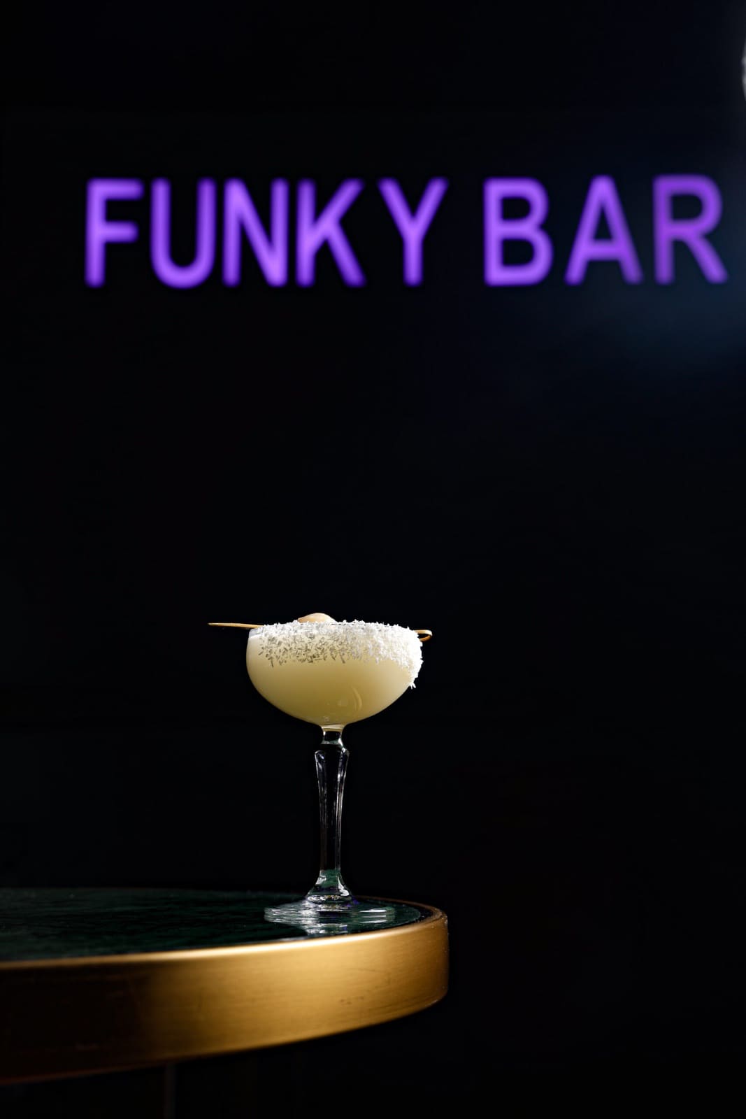A cocktail on a gold-edged table under the purple Funky Bar neon